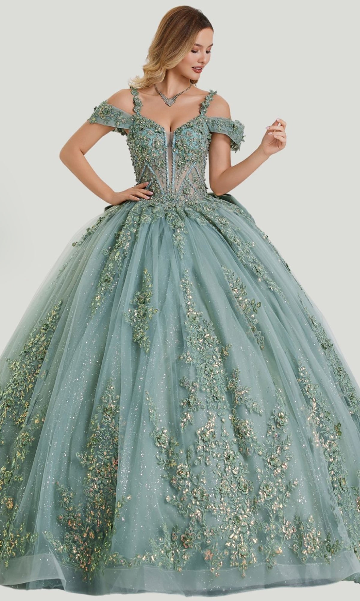 A woman wearing the Quinceanera Dress 26403 by Stella Couture in sage, showcasing an off-shoulder embellished corset bodice with sparkling accents, delicate floral appliqué, and a full glitter tulle skirt.